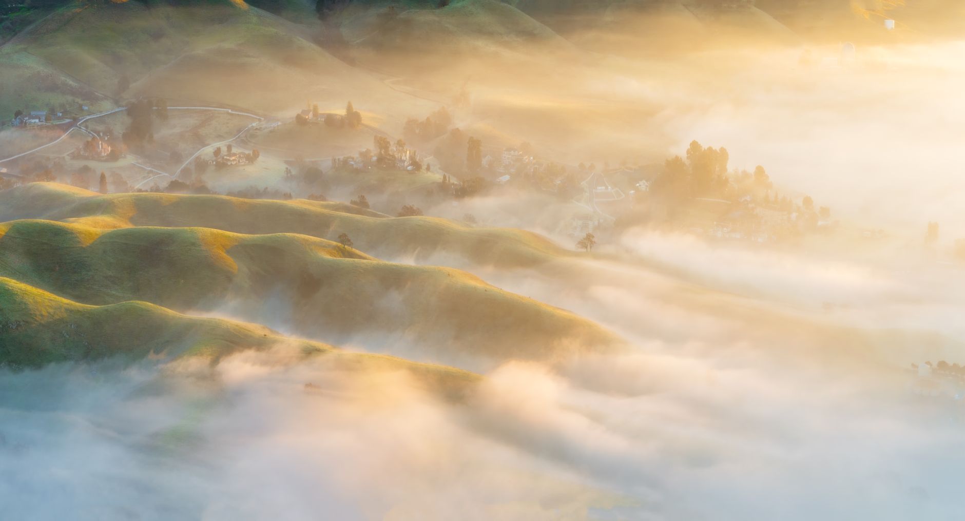 Golden morning light and low fog drifting through rolling green hills and valleys
