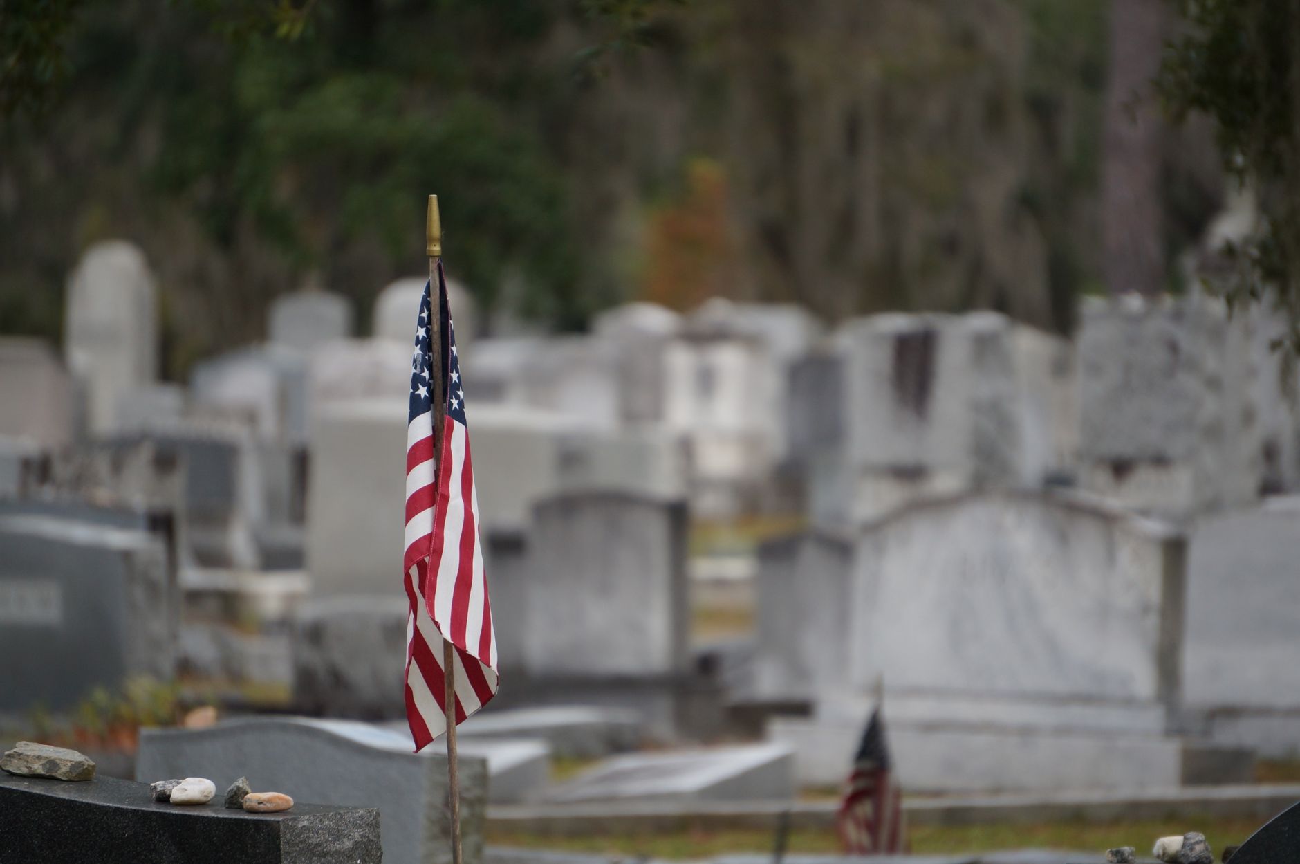 A small American flag among blurred white headstones in a quiet cemetery