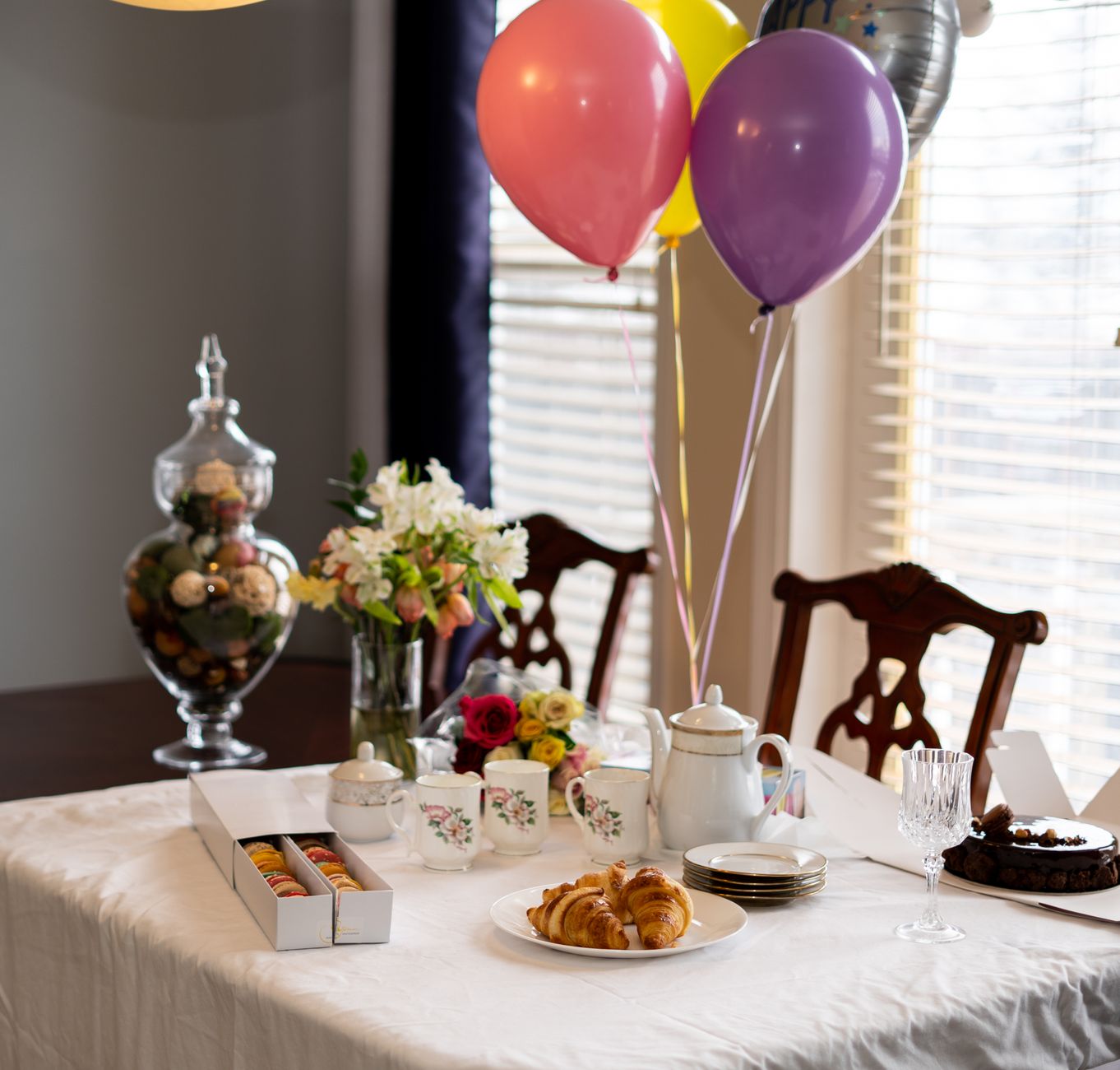A holiday table set with balloons, pastries, a tea set, and a small flower arrangement