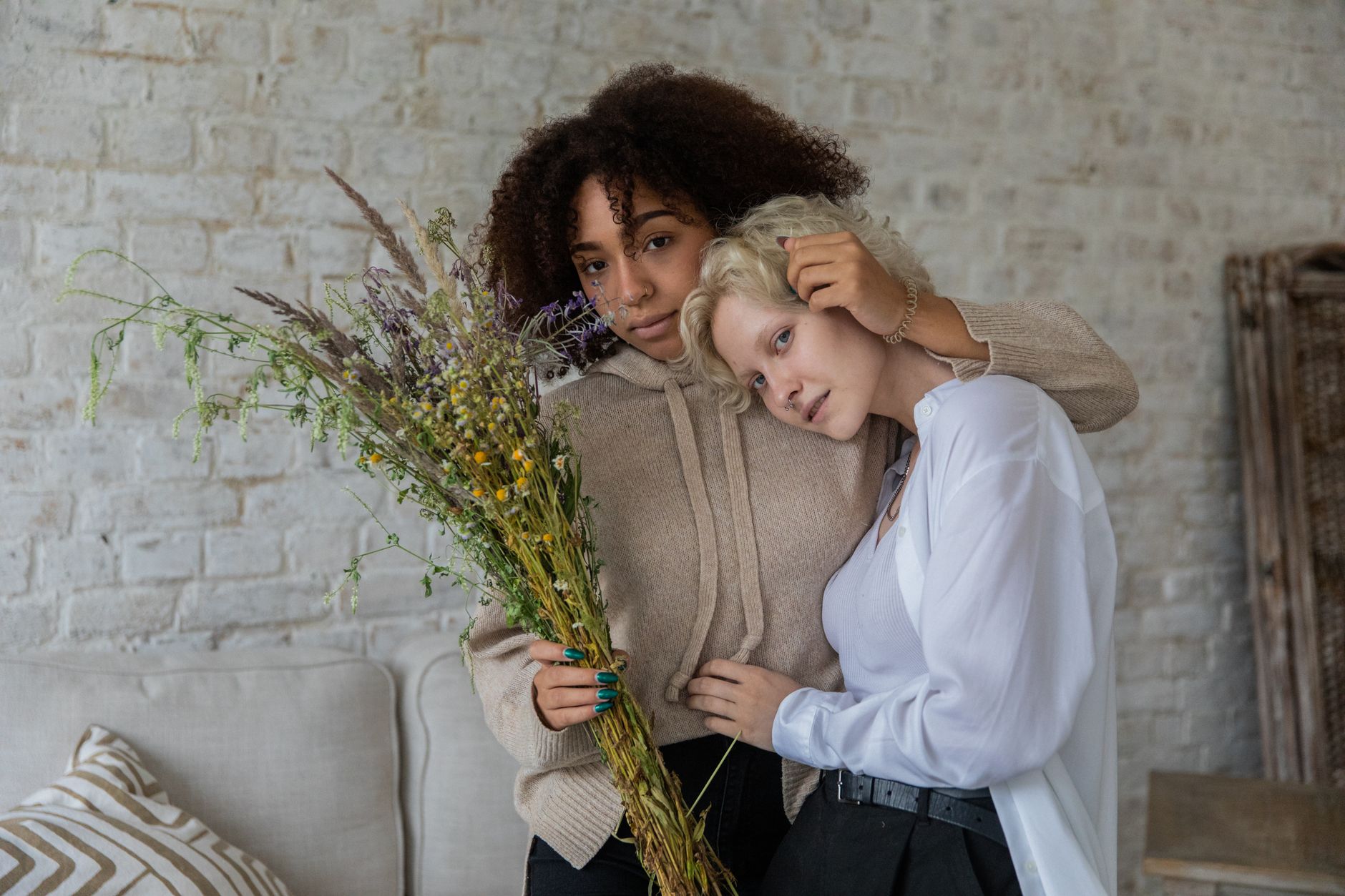 Two women embracing indoors while one holds a bundle of wildflowers