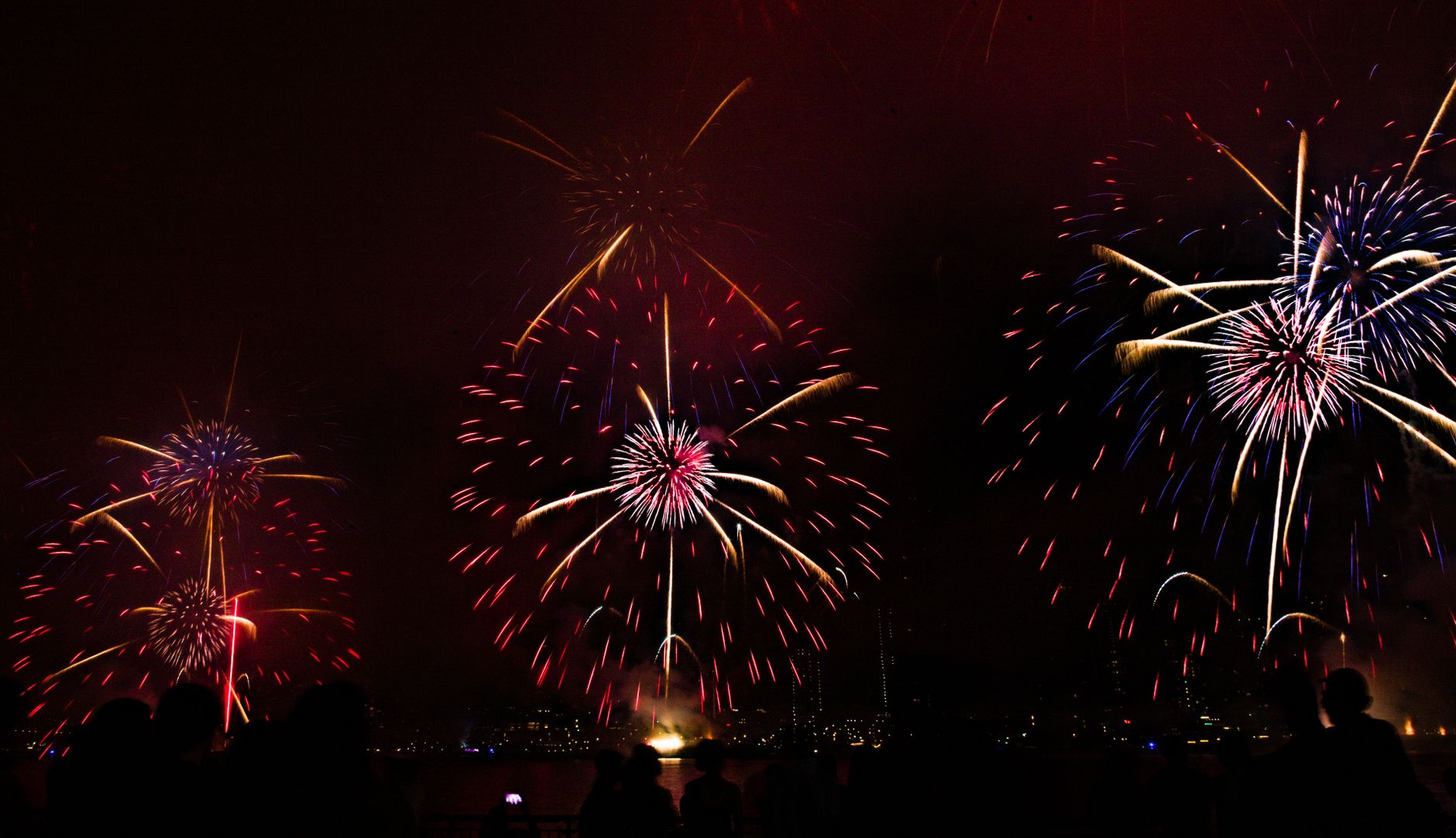 Colorful fireworks bursting over a city skyline at night with silhouetted spectators