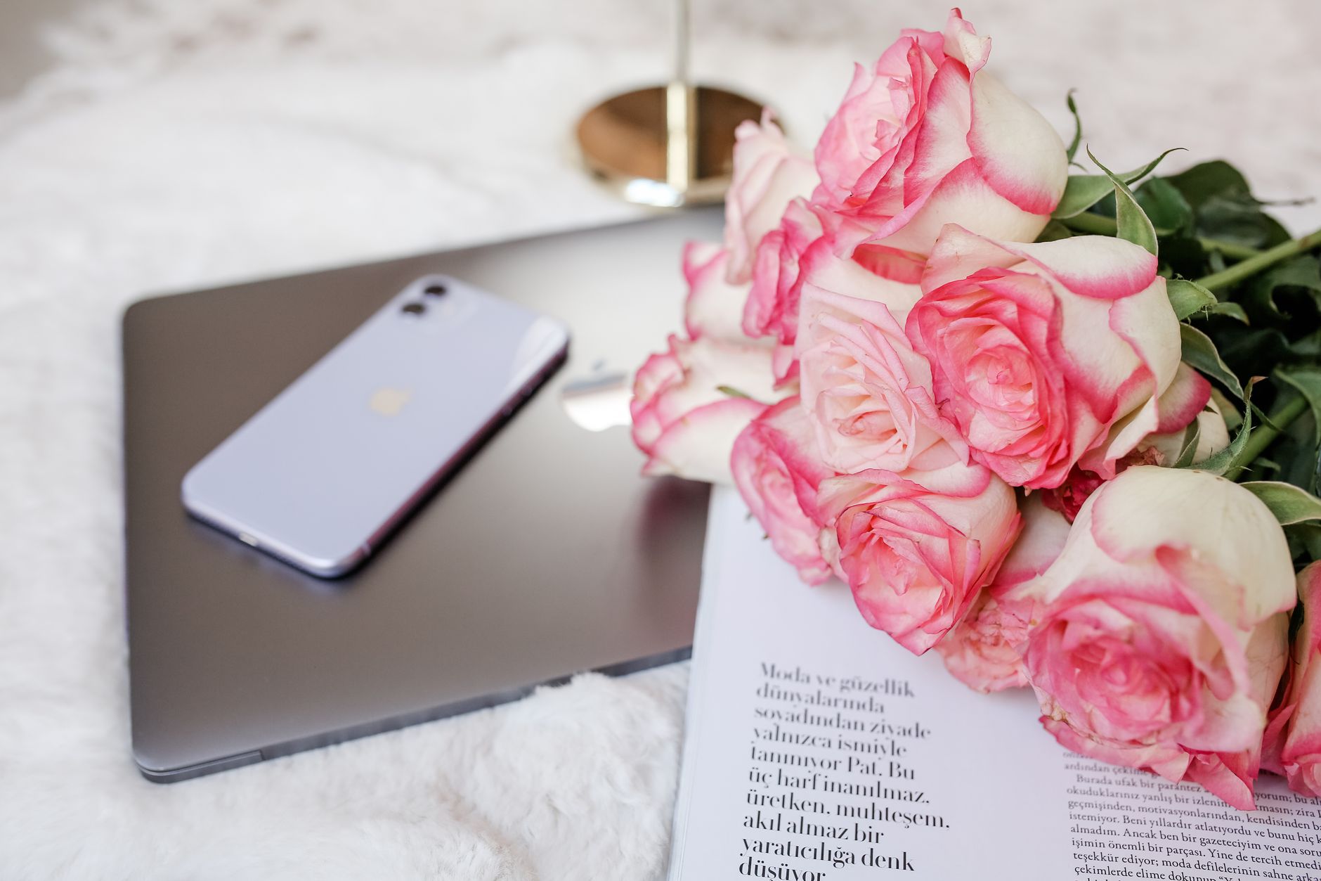 A bouquet of pink and white roses next to a laptop and phone, celebrating good news at work