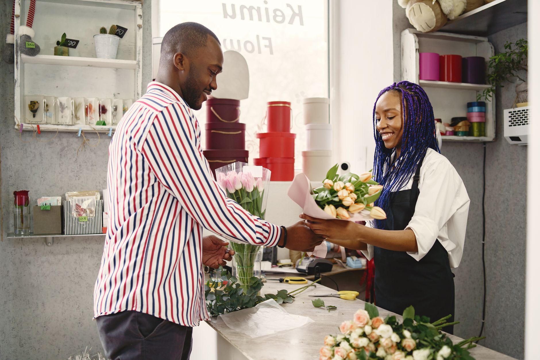 A florist handing a customer a wrapped bouquet of pink and peach tulips across the counter