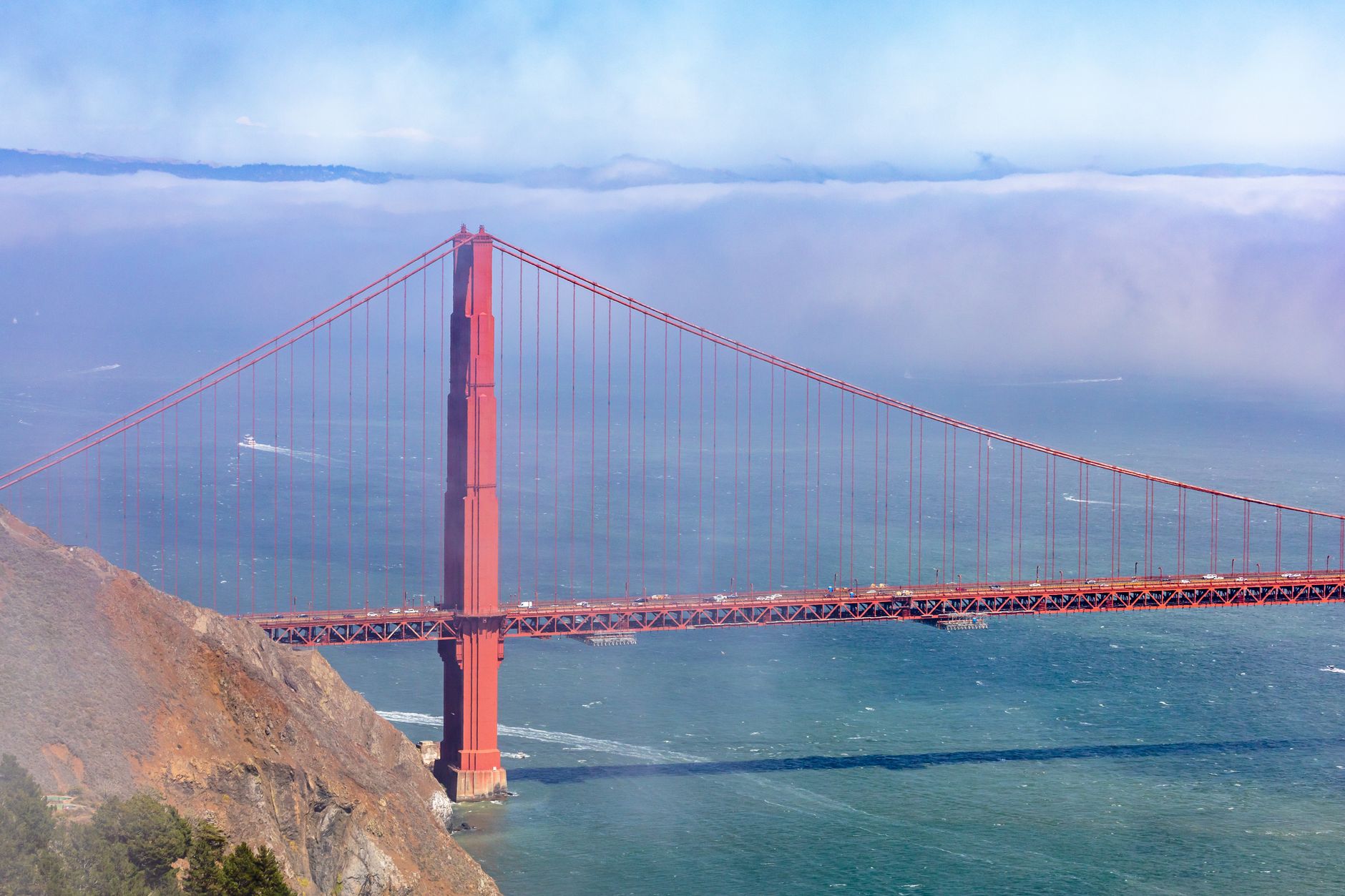 The Golden Gate Bridge spanning blue-green water with low fog drifting across the bay behind it